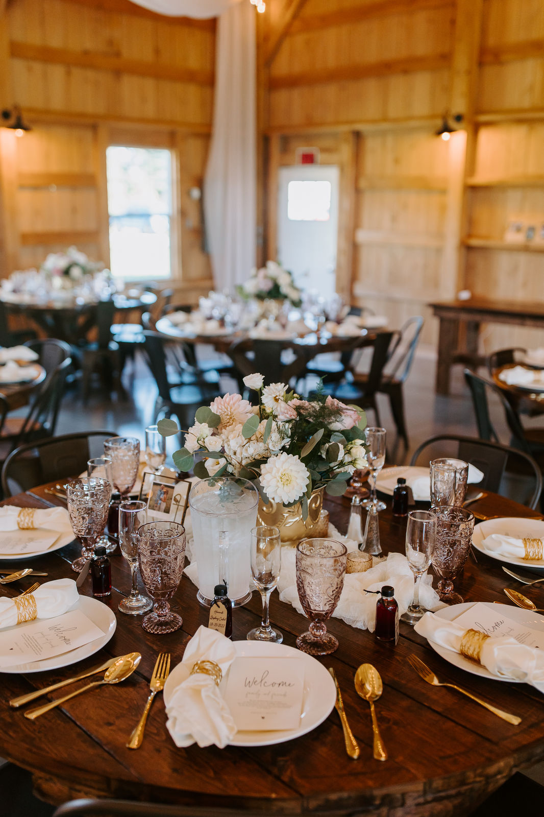 Rustic barn reception with round wood tables and warm string lights at Sunset Meadows